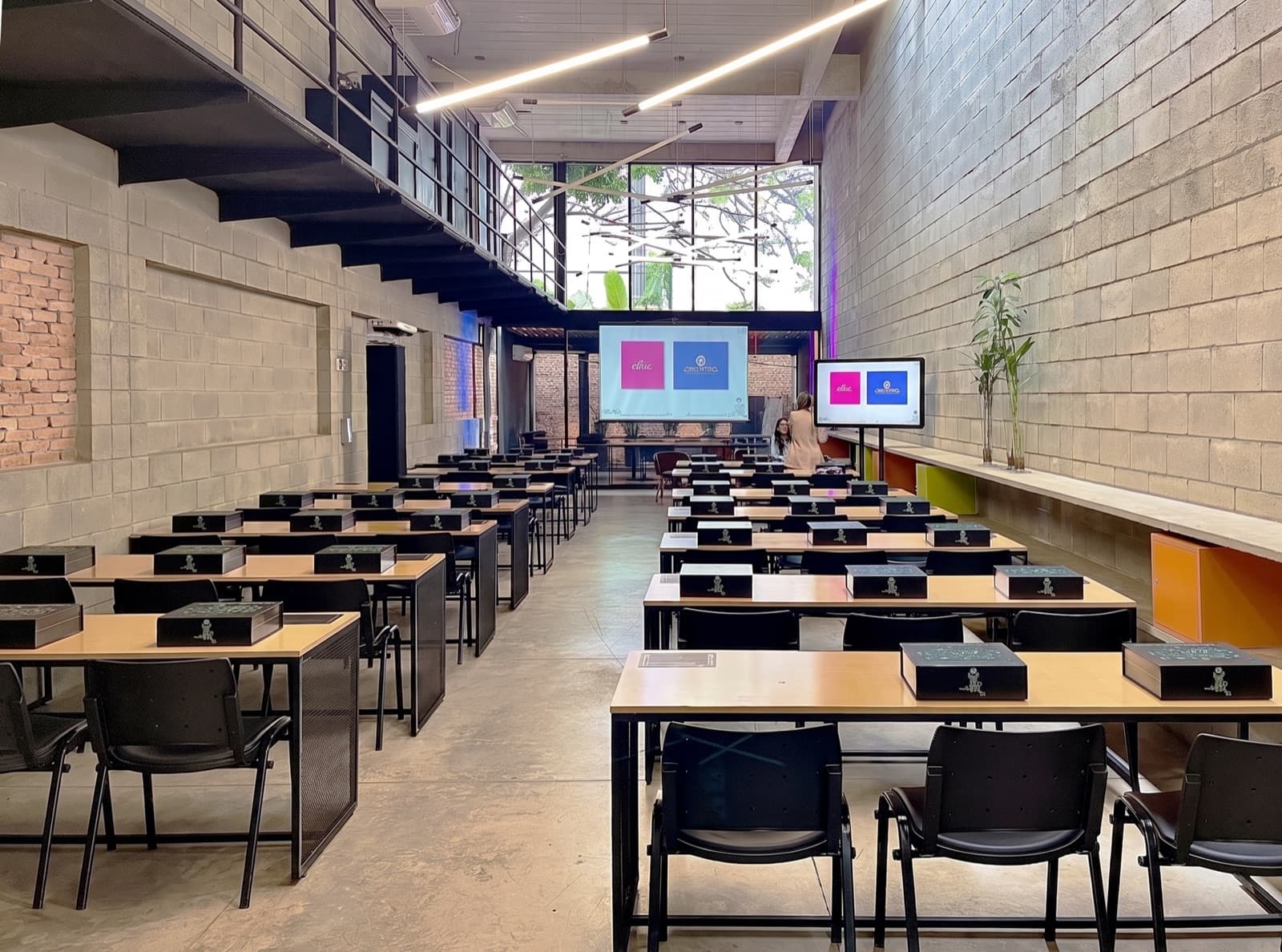 Espaço interno da Usina Colab: pé-direito duplo, paredes de bloco aparente e mesas montadas para oficina